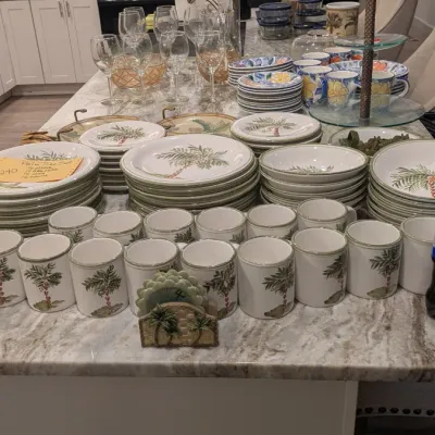 Sale Photo Thumbnail #7: Large set of palm tree-themed dinnerware, including plates, bowls, and mugs, displayed alongside glassware and serving pieces on a kitchen island.