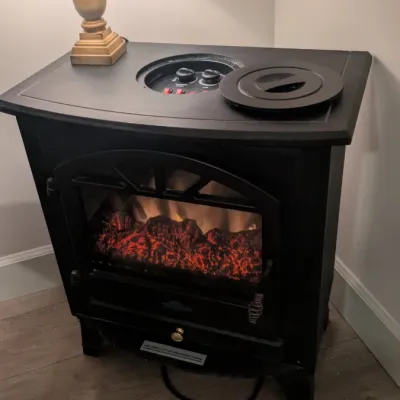Sale Photo Thumbnail #37: Black electric fireplace stove heater with a faux-log flame effect, featuring top-mounted controls under a removable lid.