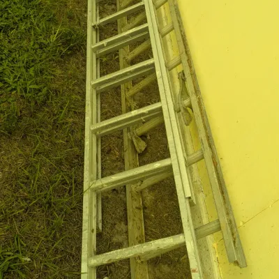 Sale Photo Thumbnail #89: Vintage aluminum extension ladder leaning against a yellow exterior wall, showing signs of outdoor use.