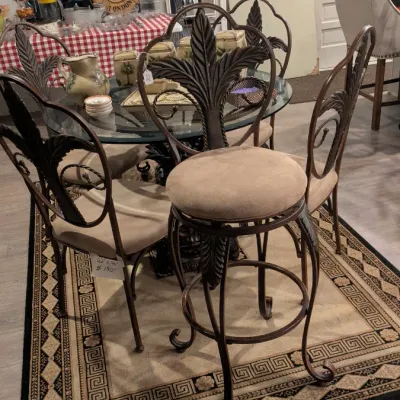Sale Photo Thumbnail #6: Wrought iron dining set featuring a glass-top table and four matching chairs with decorative leaf-motif backs and tan upholstered seats, positioned on a patterned area rug.