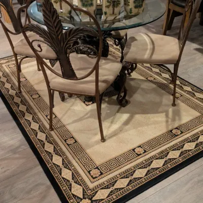 Sale Photo Thumbnail #5: Five-piece dining set featuring a round glass-top table with a decorative metal base and four matching metal chairs with palm leaf backrests and beige upholstered seats, positioned over a Greek key patterned area rug.