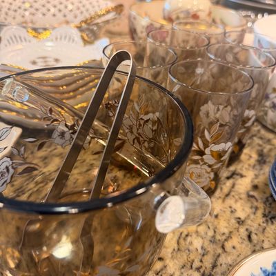 Sale Photo Thumbnail #136: Vintage mid-century amber glass ice bucket with matching tumblers, featuring a delicate white and gold floral pattern.