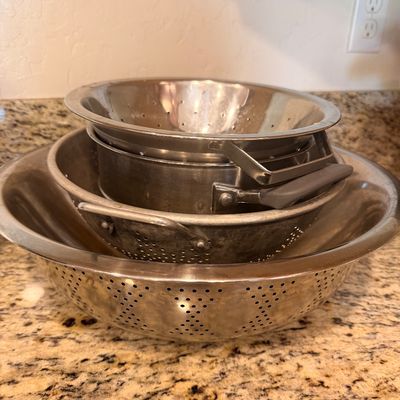 Sale Photo Thumbnail #140: Stack of four vintage and modern stainless steel and aluminum colanders in various sizes, showing some wear from use.