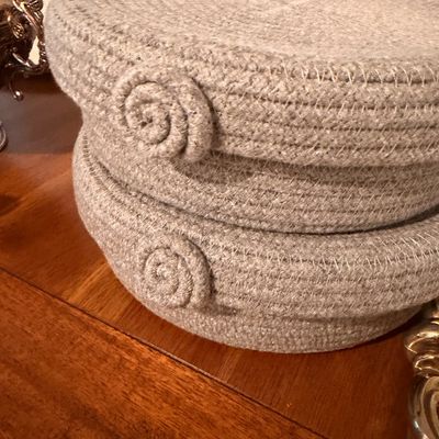 Sale Photo Thumbnail #51: Pair of round, grey woven rope storage baskets with spiral decorative details, stacked on a wooden table.