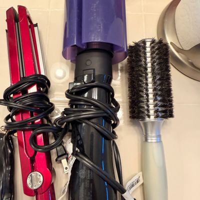 Sale Photo Thumbnail #108: Assortment of hair styling tools including a red flat iron, a purple automatic curling wand, and a round styling brush.