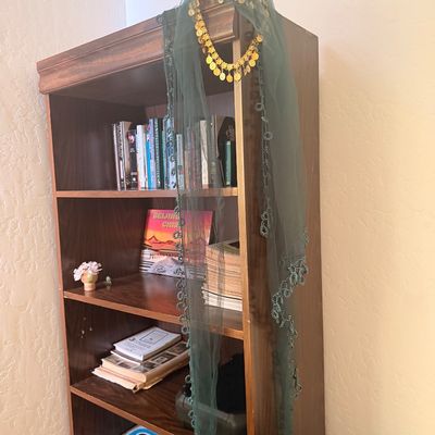 Sale Photo Thumbnail #103: Traditional green mesh headscarf with gold coin trim and beaded edges, draped over a wooden bookshelf containing books and board games.