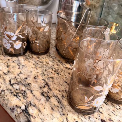 Sale Photo Thumbnail #80: Vintage mid-century smoky brown glassware set featuring white and gold floral designs, including tumblers and a matching ice bucket.