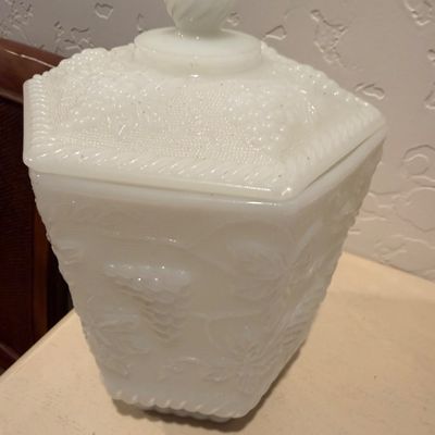 Sale Photo Thumbnail #59: Vintage milk glass lidded canister featuring a raised grape and leaf pattern, complete with a matching lid and decorative finial.