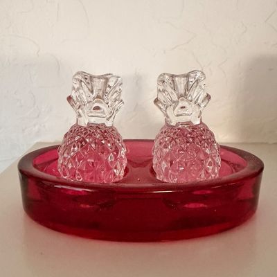 Sale Photo Thumbnail #13: Vintage clear pressed glass pineapple-shaped salt and pepper shakers sitting in a matching ruby red glass holder tray.