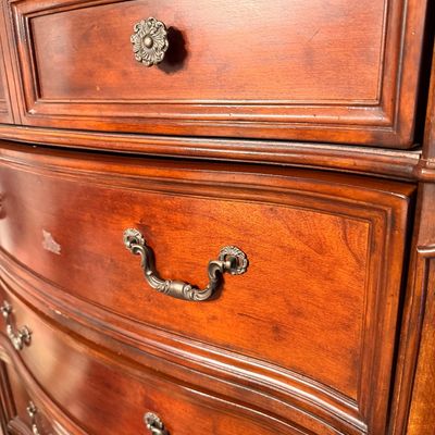 Sale Photo Thumbnail #19: Traditional cherry wood bowfront dresser featuring ornate brass bail pulls and a single decorative rosette knob on the top drawer.
