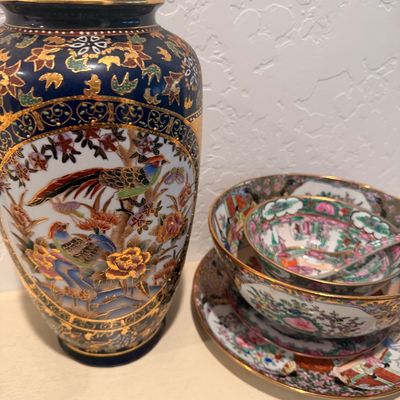 Sale Photo Thumbnail #127: Satsuma-style cobalt blue and gold gilt vase featuring a bird and floral motif, shown alongside a nested set of Famille Rose porcelain bowls and plates.