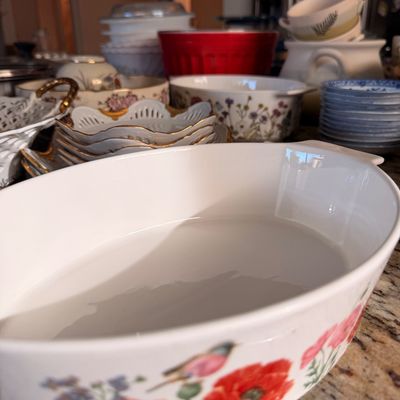 Sale Photo Thumbnail #69: Assorted ceramic kitchenware and serving dishes, featuring a white oval casserole dish with a red poppy and bird motif in the foreground.