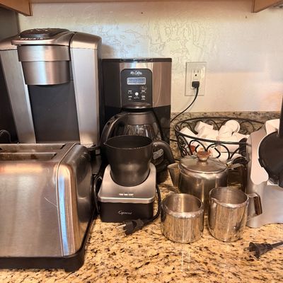 Sale Photo Thumbnail #138: Assorted kitchen appliances including a Keurig single-serve coffee maker, a Mr. Coffee drip coffee maker, a Capresso milk frother, a stainless steel toaster, and various coffee accessories on a granite countertop.