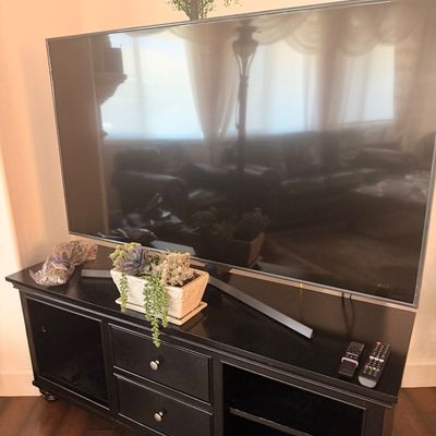 Sale Photo Thumbnail #92: Large flat-screen television on a black wooden media console with drawers and open shelving.