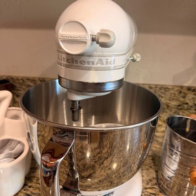 Sale Photo Thumbnail #76: White KitchenAid Artisan tilt-head stand mixer with a polished stainless steel mixing bowl, shown on a granite countertop.