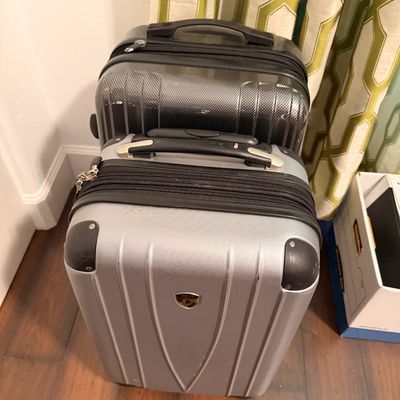 Sale Photo Thumbnail #3: Two hard-shell rolling suitcases, including a silver Heys carry-on and a larger black carbon-fiber textured suitcase, showing minor signs of wear.