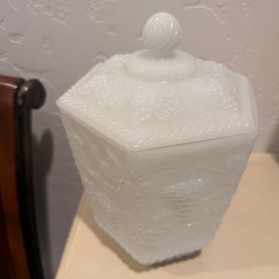 Sale Photo Thumbnail #126: Vintage milk glass lidded canister featuring an embossed grape and leaf pattern on a hexagonal body.