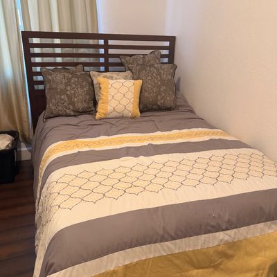 Sale Photo Thumbnail #119: Contemporary wooden bed frame with a slatted headboard, dressed in a grey, yellow, and white patterned comforter set with matching decorative pillows.
