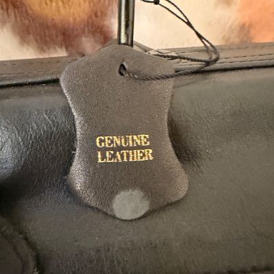 Sale Photo Thumbnail #104: Close-up of a black leather bag featuring a "Genuine Leather" tag embossed with gold lettering.