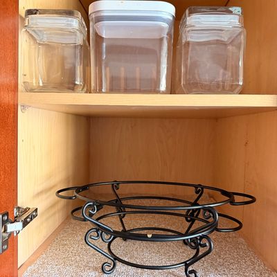 Sale Photo Thumbnail #11: Assorted kitchen storage containers including glass jars with lids and a plastic canister, alongside a black wrought iron plate or bowl stand, displayed inside a wooden cabinet.