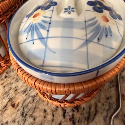 Sale Photo Thumbnail #72: Ceramic covered casserole dish featuring a blue and white plaid pattern with floral accents, resting in a fitted woven wicker basket holder.