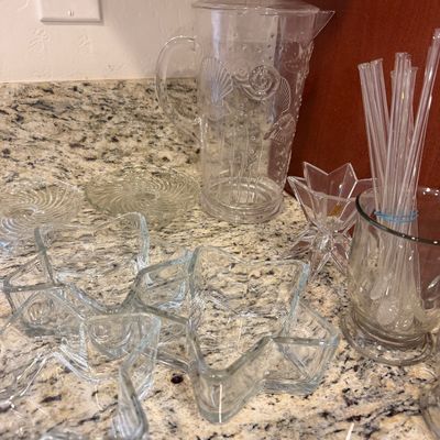 Sale Photo Thumbnail #144: Assorted clear glassware collection, including star-shaped bowls, a plastic pitcher with embossed seashell designs, glass stirrers, and small plates.