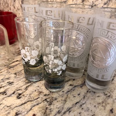 Sale Photo Thumbnail #150: Assorted vintage souvenir shot glasses, including frosted glasses featuring Cancun motifs and clear glasses with white floral designs.