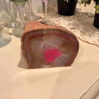 Sale Photo Thumbnail #53: Polished agate geode slice with a vibrant pink dyed center, showing natural crystalline structures and a rough outer rind.