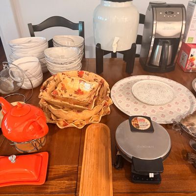 Sale Photo Thumbnail #95: Assorted kitchenware and small appliances, including a Cuisinart coffee maker, a waffle maker, a ceramic beverage dispenser, stacks of bowls, and an orange teapot with matching butter dish.