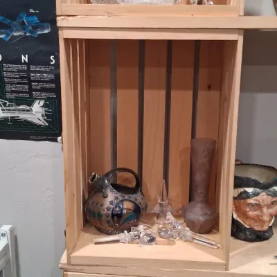 Assorted glassware and collectibles displayed on wooden crate shelving, including a cut glass decanter, a lidded candy dish, a Royal...