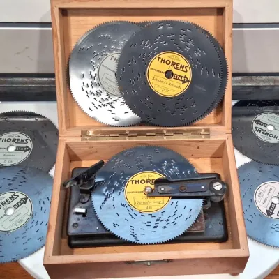 Vintage Thorens disc music box housed in a simple wooden case, accompanied by six interchangeable metal music discs featuring classical...