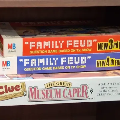 Stack of vintage board games including Milton Bradley's Family Feud 3rd and 4th editions, and Parker Brothers' Clue: The Great...