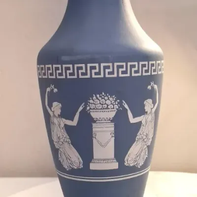 Wedgwood-style blue jasperware bud vase featuring white bas-relief classical figures flanking a floral pedestal, accented by a Greek key...