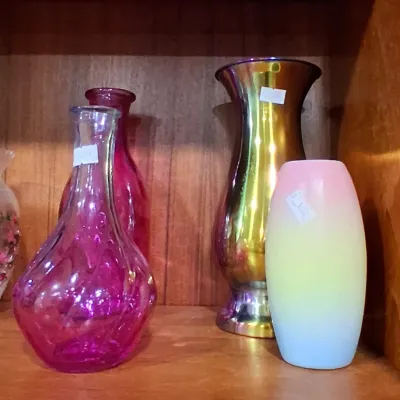 Collection of vintage glass vases, including a textured magenta glass decanter, a tall metallic gold-toned iridescent vase, and a pastel...
