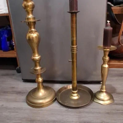 Three vintage brass candlesticks of varying heights and styles, including a tall baluster-stem holder, an adjustable push-up candlestick...