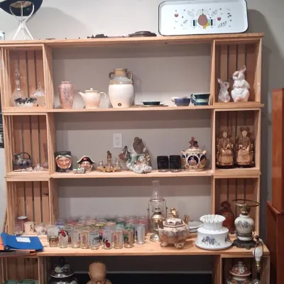A large wooden crate shelving unit displaying an assortment of vintage collectibles, including glassware, ceramic figurines, pottery,...