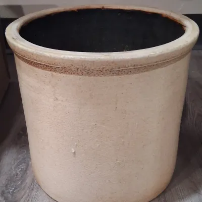 Antique salt-glazed stoneware crock featuring a dark brown interior glaze and a simple, unadorned beige exterior with a thick rim.