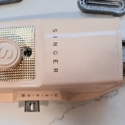 Vintage Singer automatic buttonholer attachment in a beige casing, featuring a textured gold-tone faceplate and adjustable width settings.
