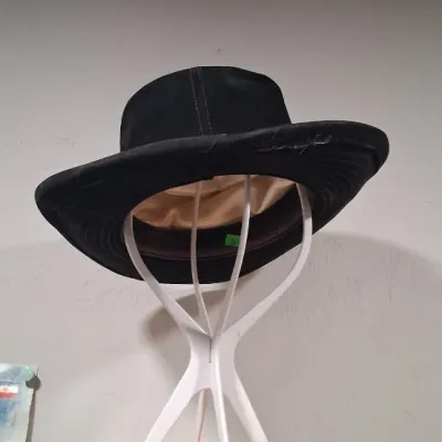 Vintage black suede or brushed fabric wide-brim hat with a satin lining, displayed on a white plastic hat stand.