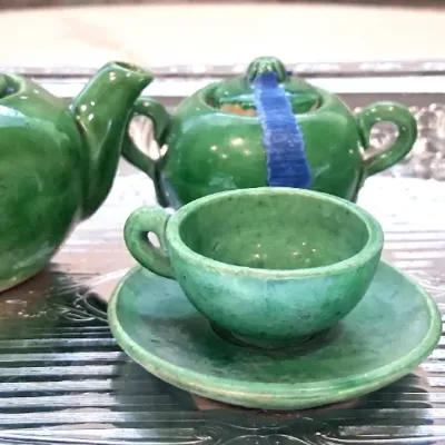 Vintage miniature green glazed ceramic tea set, including a teapot, lidded sugar bowl, creamer, and a teacup with saucer, displayed on a...