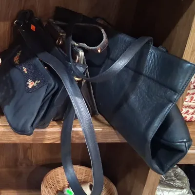 Collection of vintage black handbags, including a textured leather shoulder bag and a smaller fabric purse featuring embroidered floral...