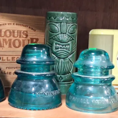 Collection of vintage items including three aqua glass insulators by Hemingray and Whitall Tatum Co., a green ceramic tiki mug, a...