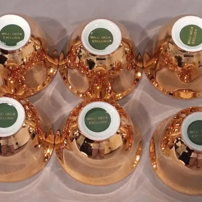 Set of six Willi Geck Exclusiv copper-toned metallic glazed porcelain cups, shown upside down to display the green maker's mark on...