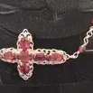 Sterling silver sideways cross necklace featuring filigree detailing and set with faceted pink tourmaline or garnet gemstones, displayed...