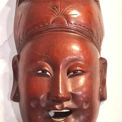 Vintage hand-carved wooden Asian mask, featuring a smiling face with a detailed headdress and a rich reddish-brown polished finish.