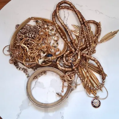 Assortment of vintage gold-toned costume jewelry, including textured link necklaces, snake chain bracelets, and a pendant with a colorful...