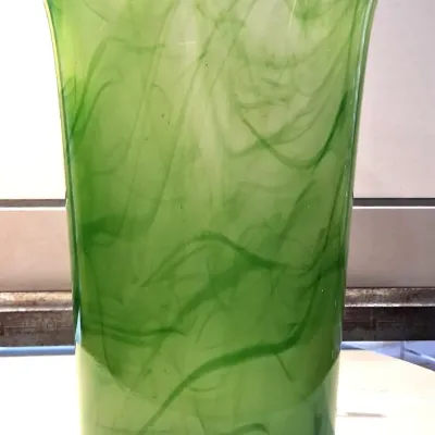 Art glass vase featuring a flared rim and a vibrant green swirl pattern throughout the translucent body.