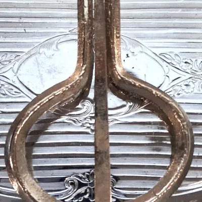 Vintage metal jaw harp, also known as a jew's harp, showing some surface wear and patina, resting on an ornate silver-plated tray.