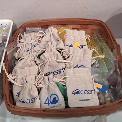 A collection of 4ocean branded linen drawstring jewelry pouches and small plastic bags filled with items, presented in a woven wooden...