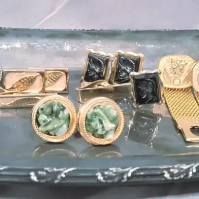 Assortment of vintage men's cufflinks and tie clips, including gold-tone, jade-style, and cameo designs, displayed on a...